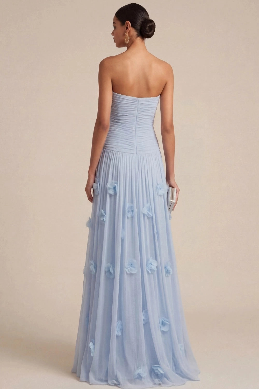 Back view of light blue strapless bridesmaid dress featuring a ruched fitted bodice, center-back zipper, dropped waist, and 3D floral appliqués on a long tulle-look skirt.
